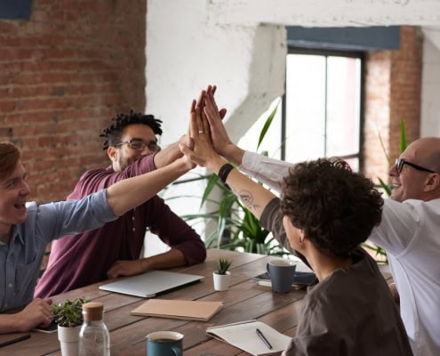 Erfolgreiches Team an einem Tisch - Themen: Sozialbeziehungen und Unternehmenskultur fördern dank INQA-Coaching